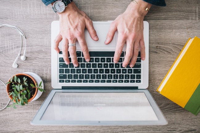 This photo shows a man typing on a laptop