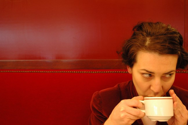 This photo shows a woman sipping coffee against a red wall and red booth