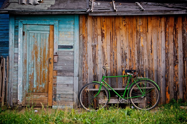This photo shows a dilapidated barn with a green bicycle leaning against its front wall.