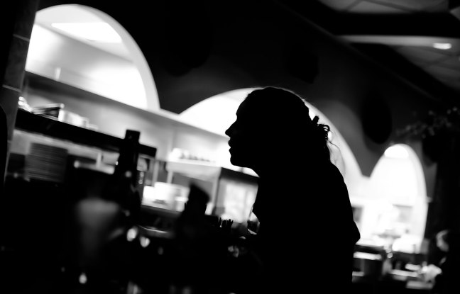 A waitress in a diner stands in profile silhouette in black and white