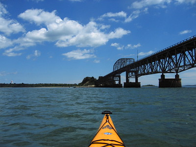 This photo shows the top of a yellow kayak heading out toward the Bridge at Long Island on Boston Harbor.