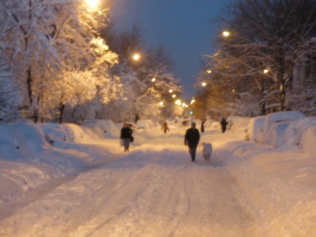 Two pedestrians walk along the sides of a snowy road in Washington, DC